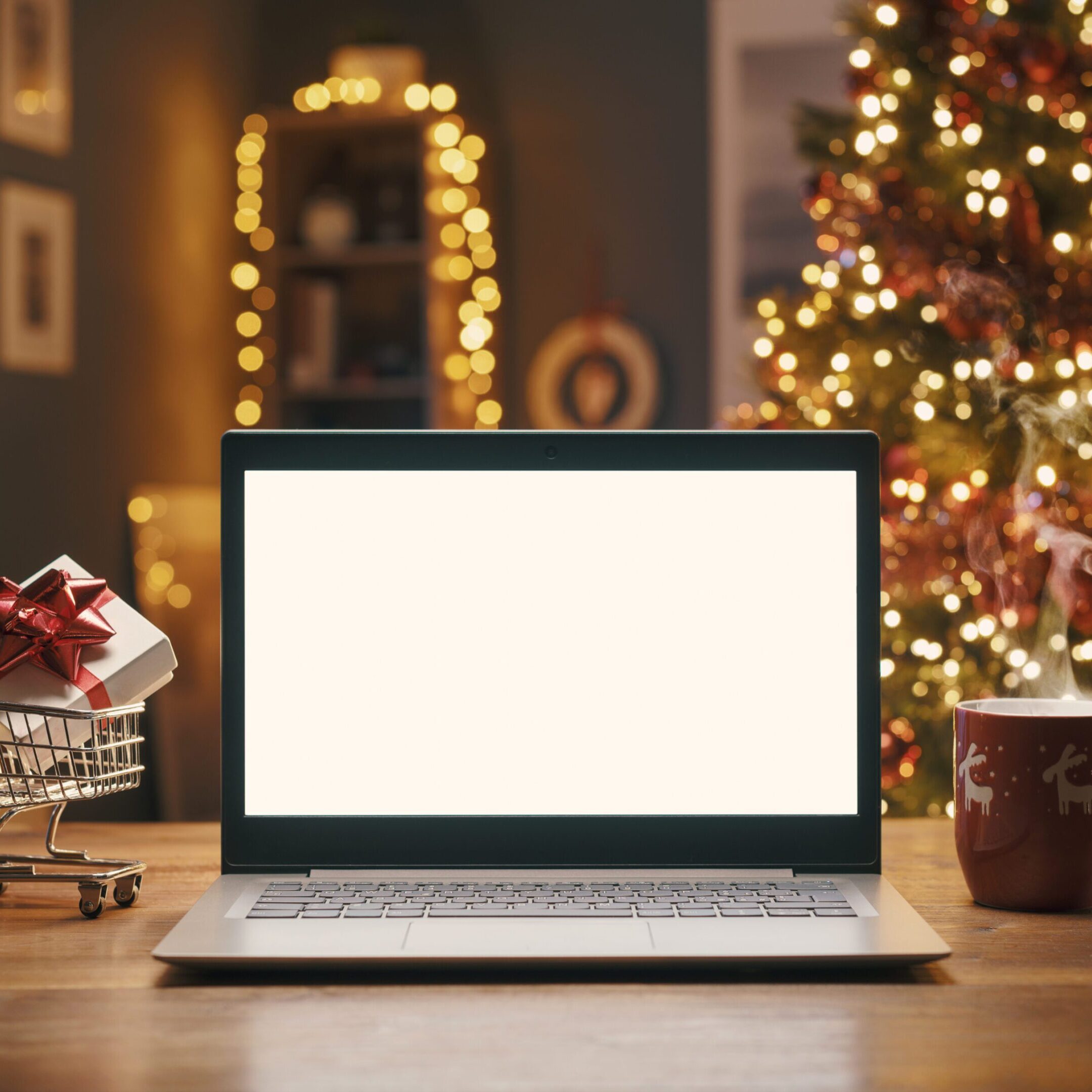 Christmas shopping online at home, laptop with blank screen and miniature shopping cart with a gift inside, holidays and sale concept